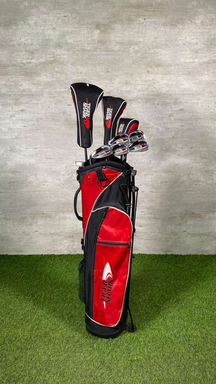 Red and black golf bag with golf clubs against a gray wall.