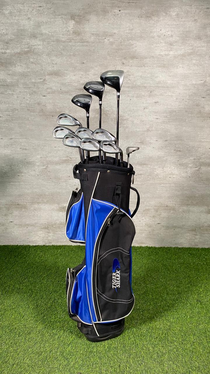 Golf club set in a black and blue bag on grass with a concrete wall background