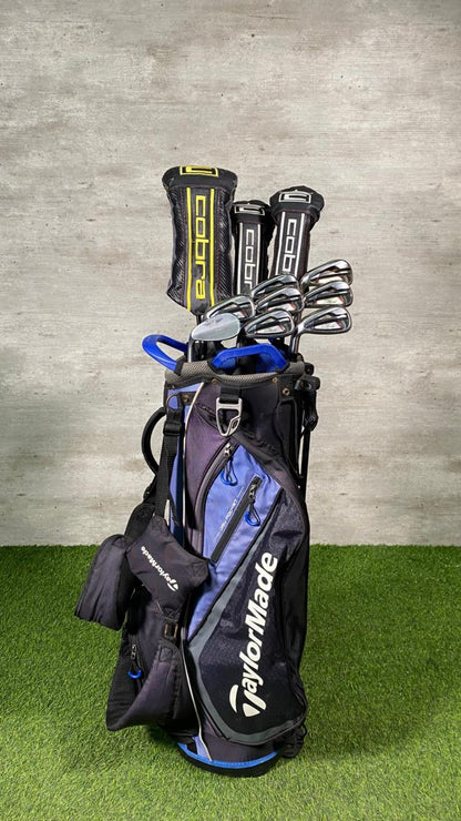 Golf clubs in a TaylorMade bag on a grass and concrete background