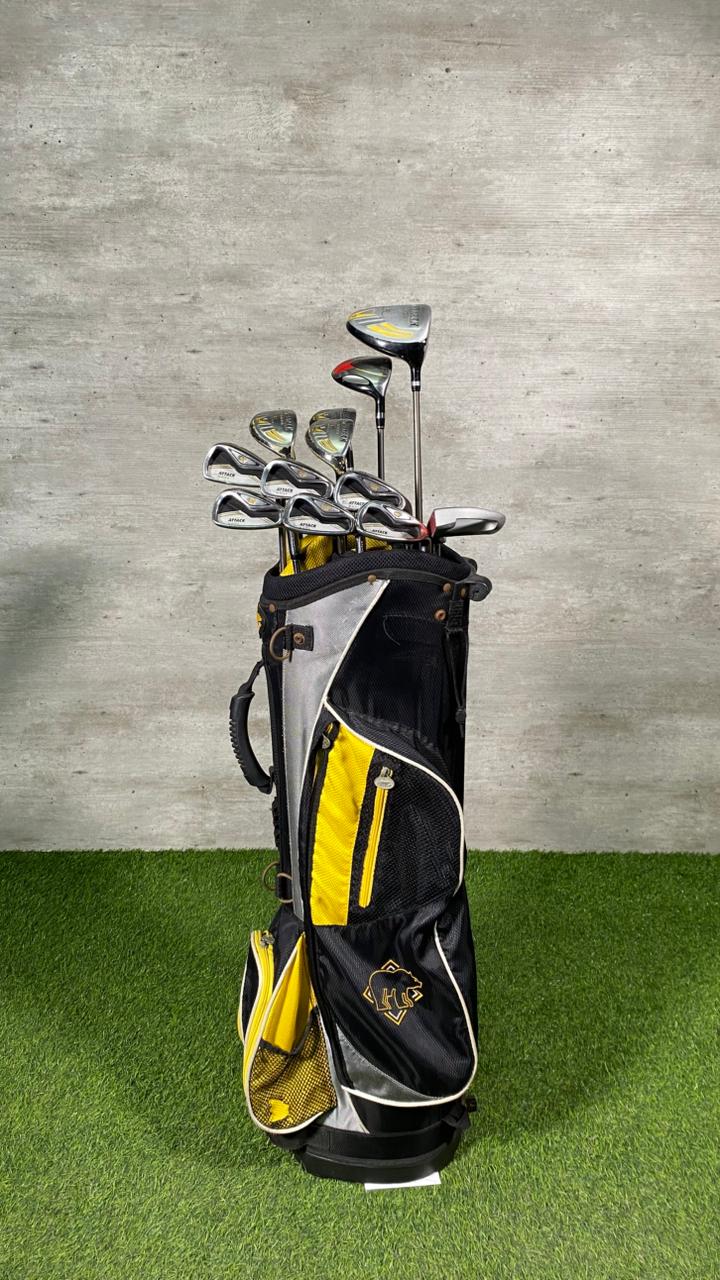 Golf clubs in a black and yellow bag on a green surface with a gray wall background
