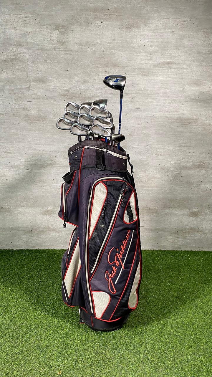 Golf bag with golf clubs on a grassy surface against a concrete wall.