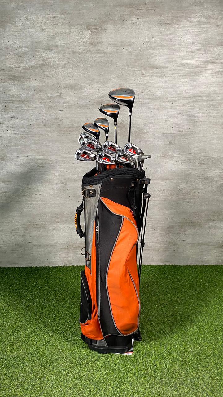 Golf clubs in an orange and black bag on a green surface with a gray concrete wall background