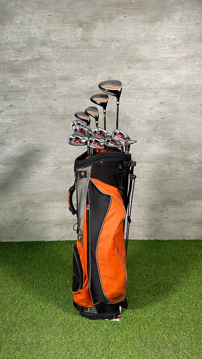 Golf clubs in an orange and black bag on a green surface with a gray concrete wall background