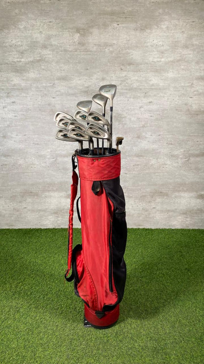 Red golf bag with golf clubs against a gray wall on green grass