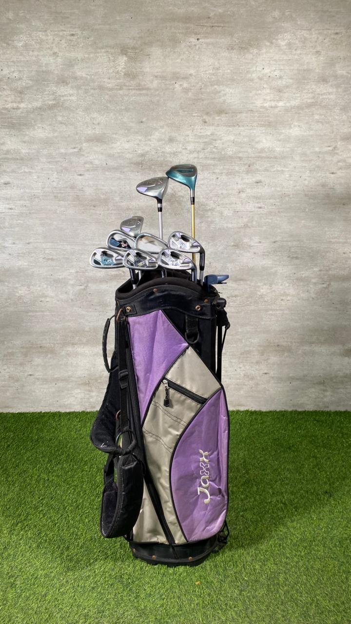 Golf bag with clubs on a grassy surface against a textured wall