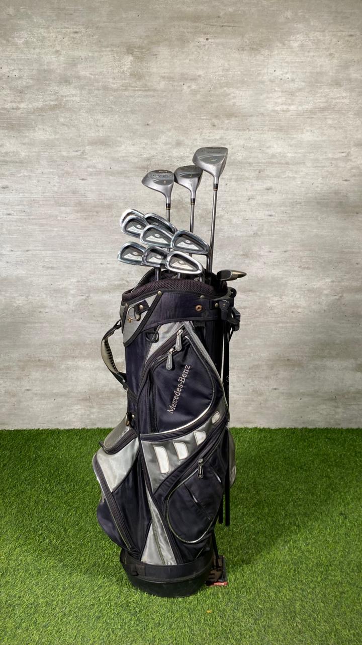 Golf clubs in a bag on a grassy surface with a concrete wall background