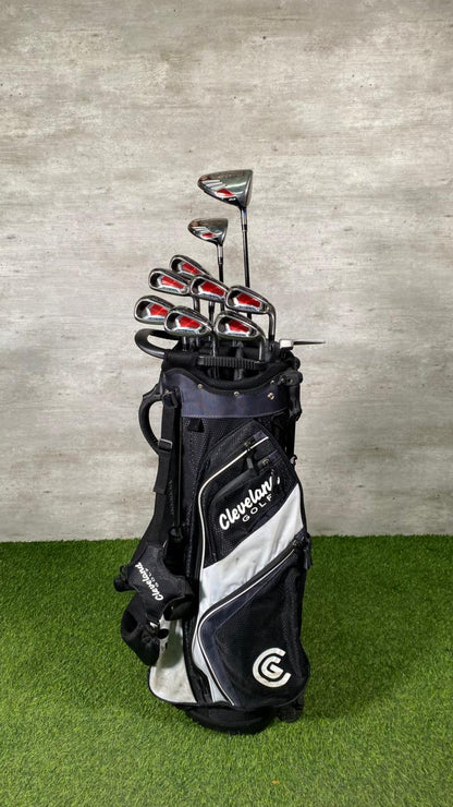 Golf clubs in a black and white bag on a grassy surface with a concrete wall background