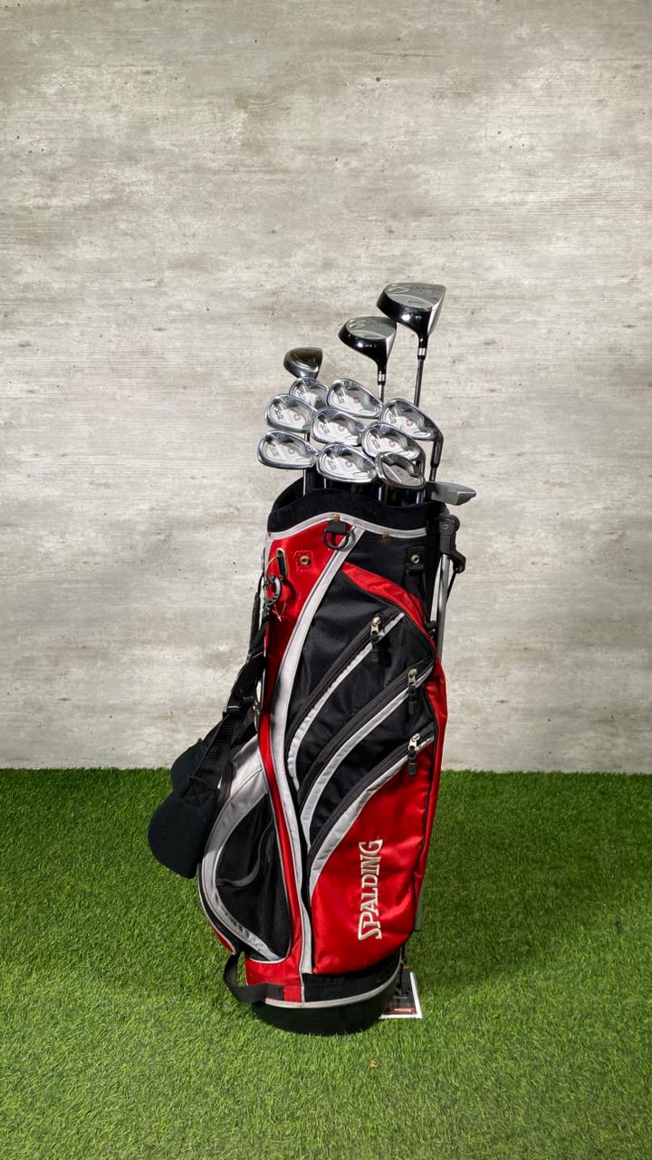 Golf bag with clubs on a grassy surface against a concrete wall