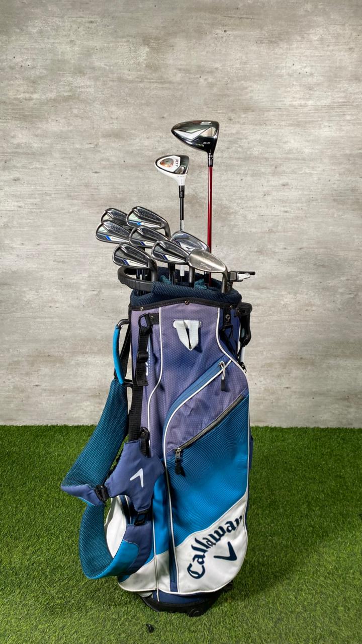 Callaway golf bag with clubs on a grassy surface against a concrete wall.