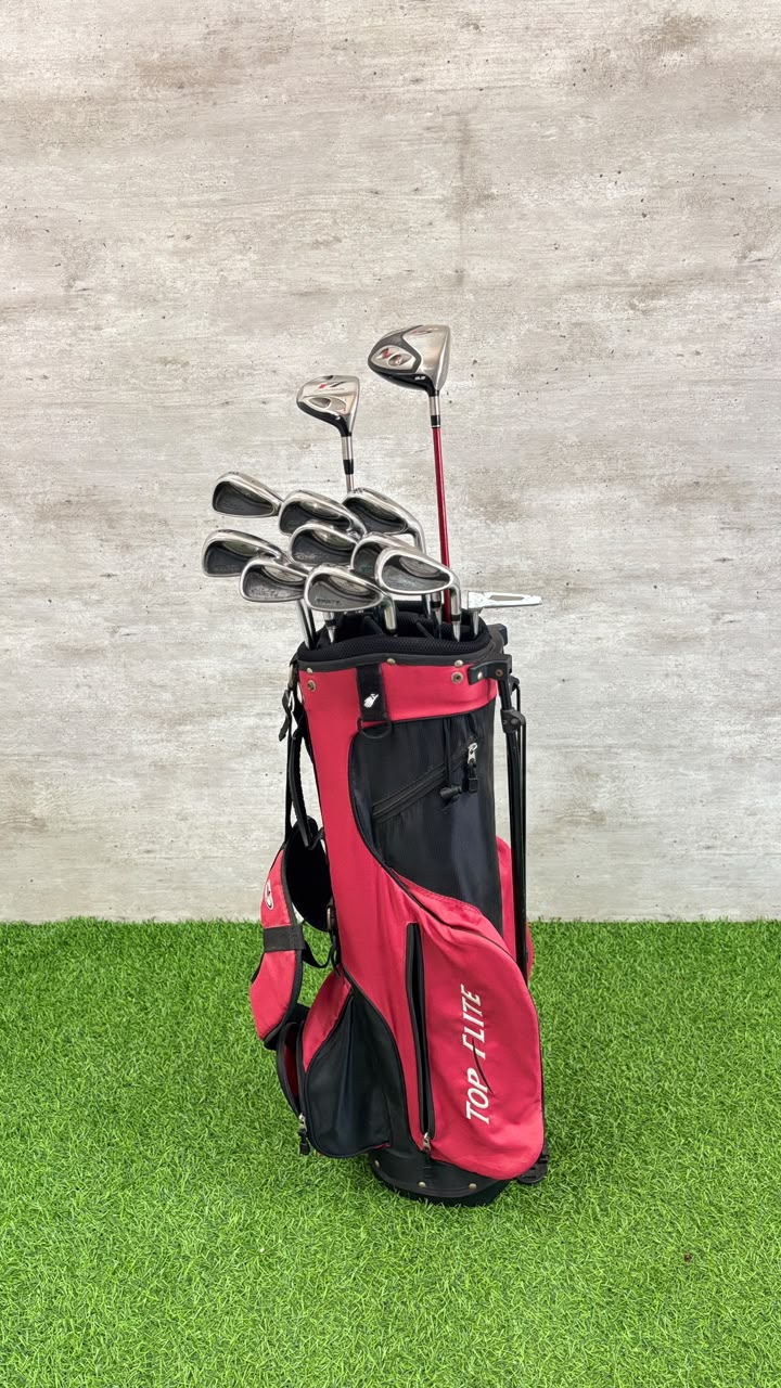 Red golf bag with golf clubs on a grassy surface and concrete wall background