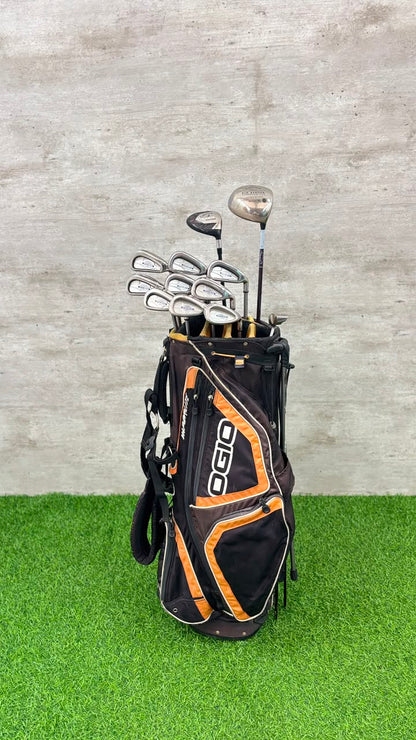Golf clubs in a black and orange Ogio bag on a green surface with a gray textured wall background