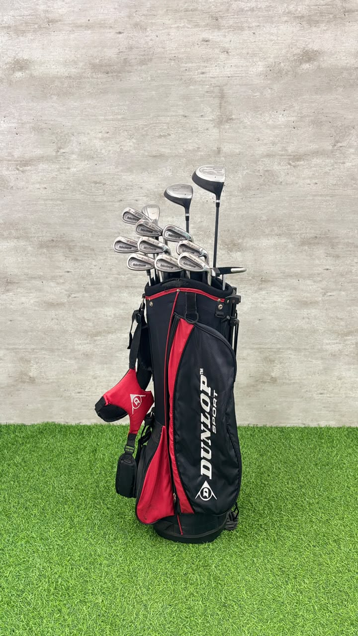 Golf clubs in a black and red Dunlop bag on grass with a concrete wall background