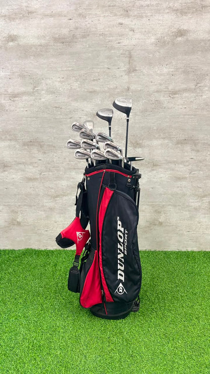 Golf clubs in a black and red Dunlop bag on grass with a concrete wall background