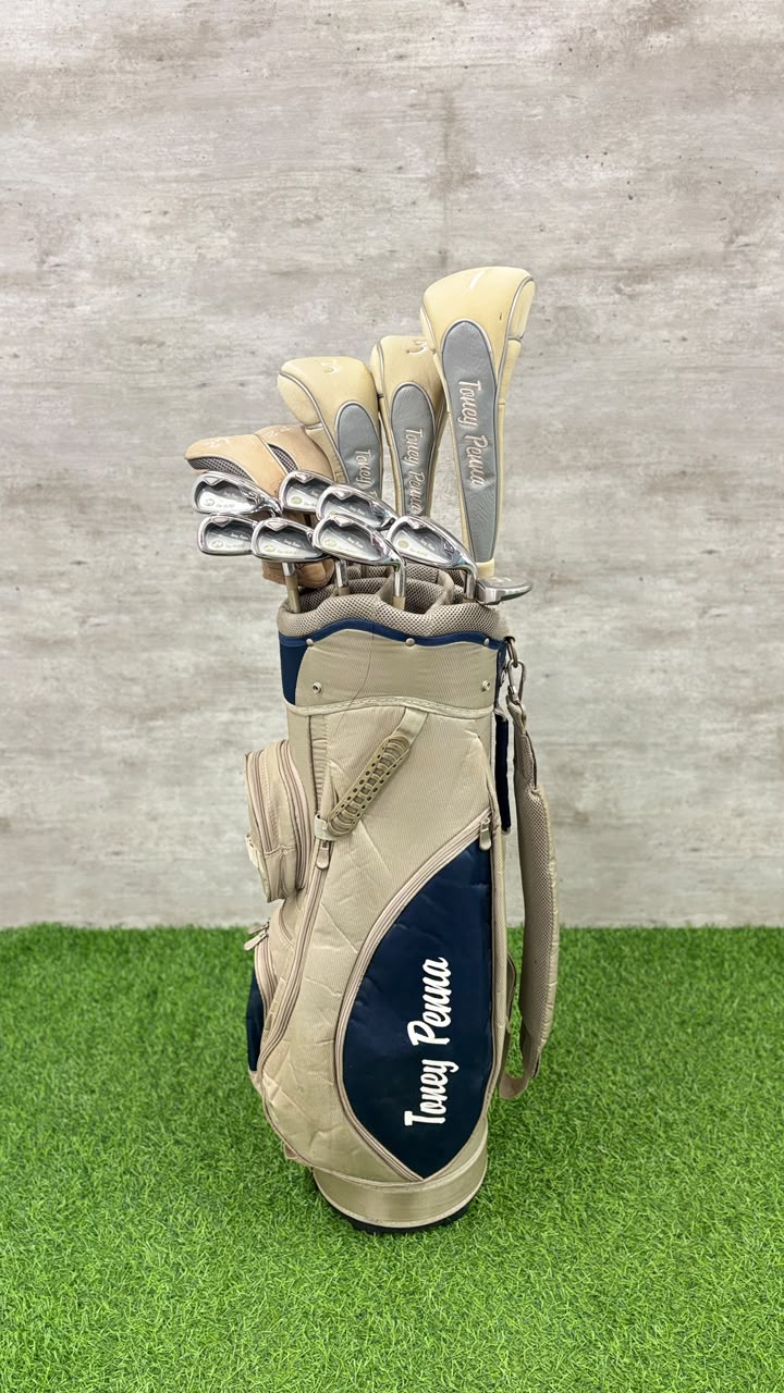 Golf club set in a beige bag with navy blue logo on grass and concrete background