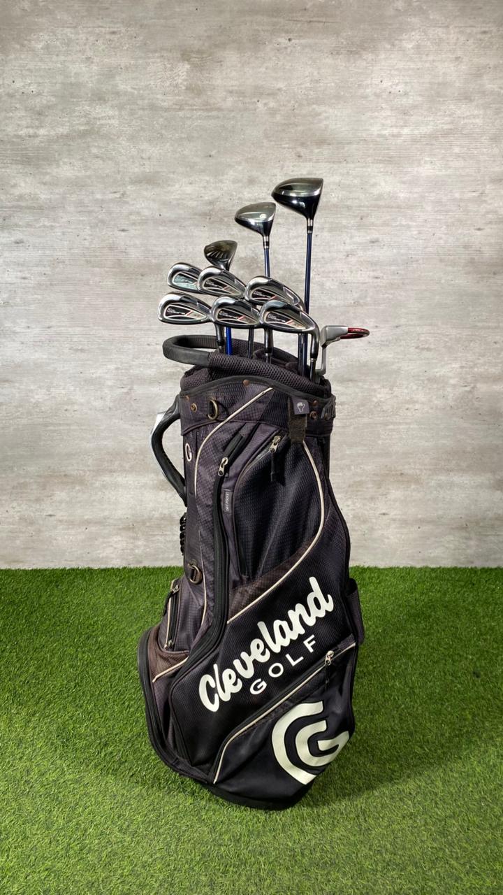 Golf bag with clubs on a grassy surface against a concrete wall