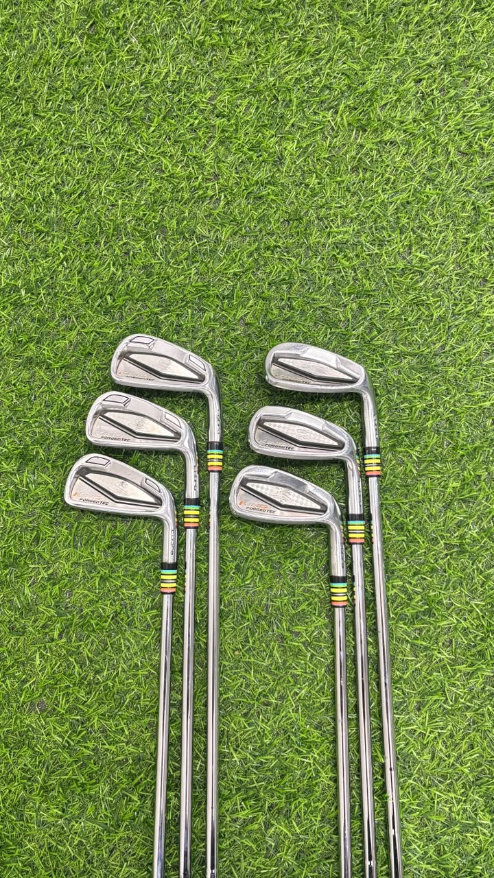 A set of eight golf iron clubs arranged in two vertical rows on a green grass surface.