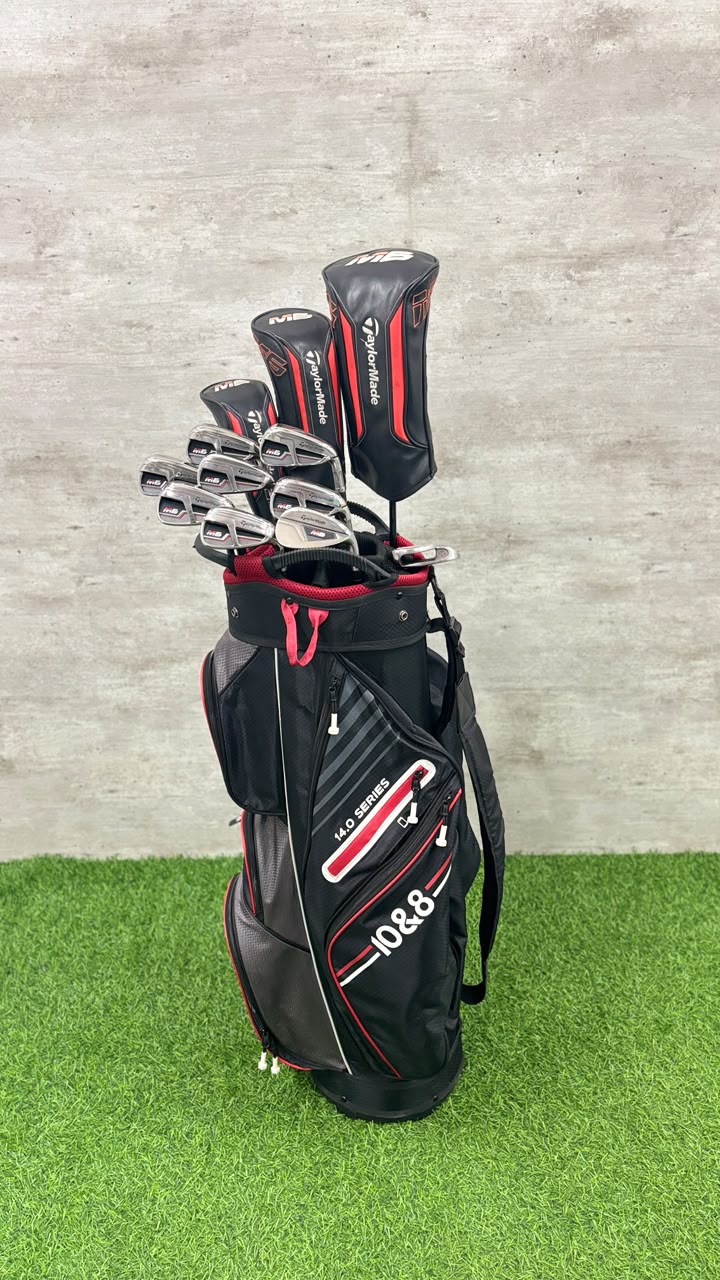 A black and red 10.5 golf club set in a matching golf bag, standing on artificial green turf against a gray concrete wall.