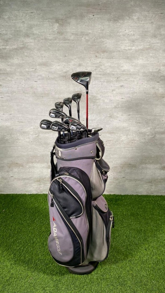 Golf bag with golf clubs on a grassy surface against a concrete wall.