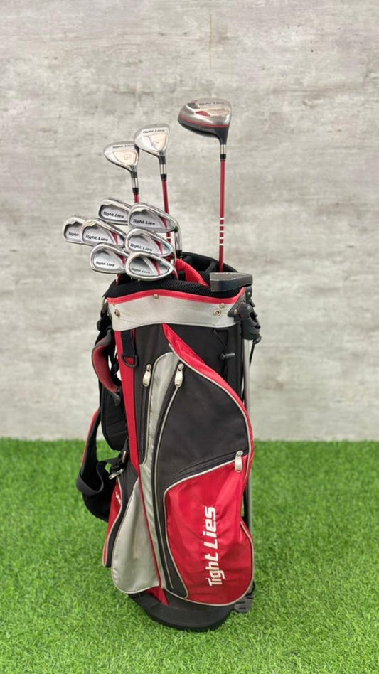 Golf clubs in a red and black bag on grass with a gray background