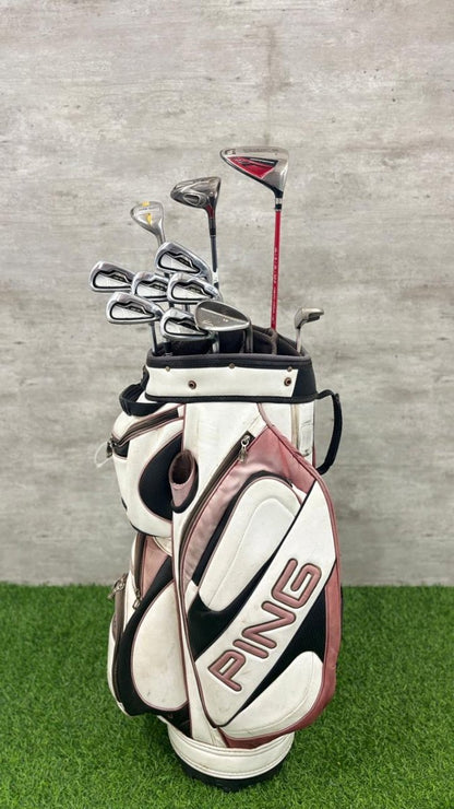 Golf bag with clubs on a grassy surface against a concrete wall.
