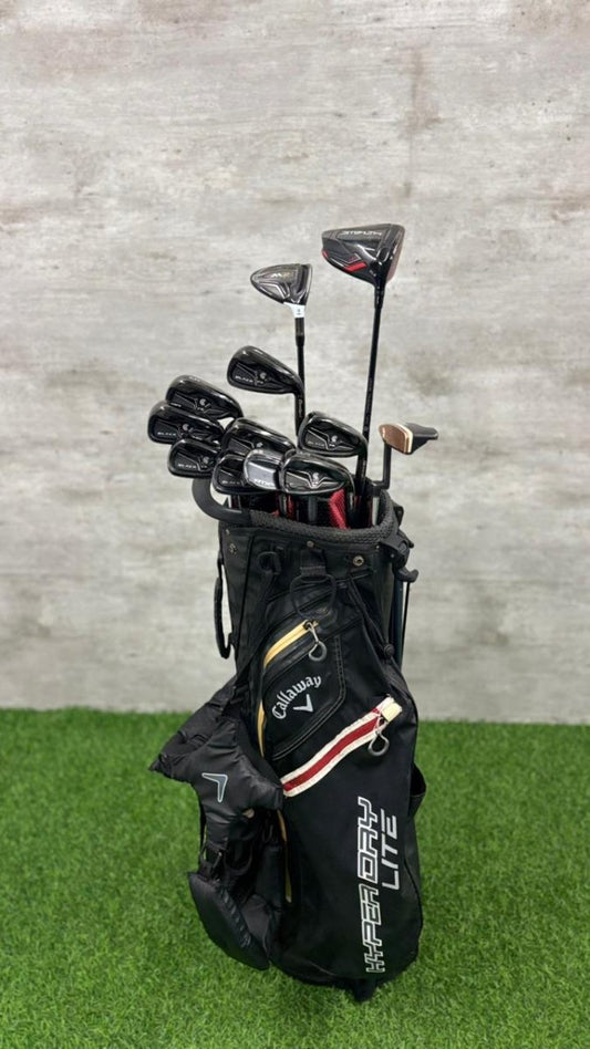 Golf clubs in a black bag on a grassy surface with a concrete wall background