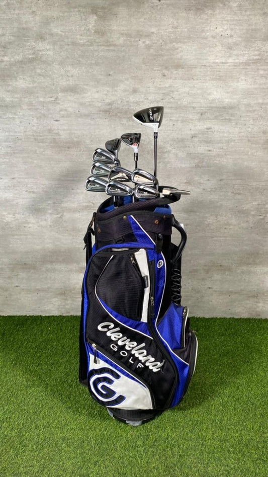 Golf bag with golf clubs on a grassy surface against a gray wall