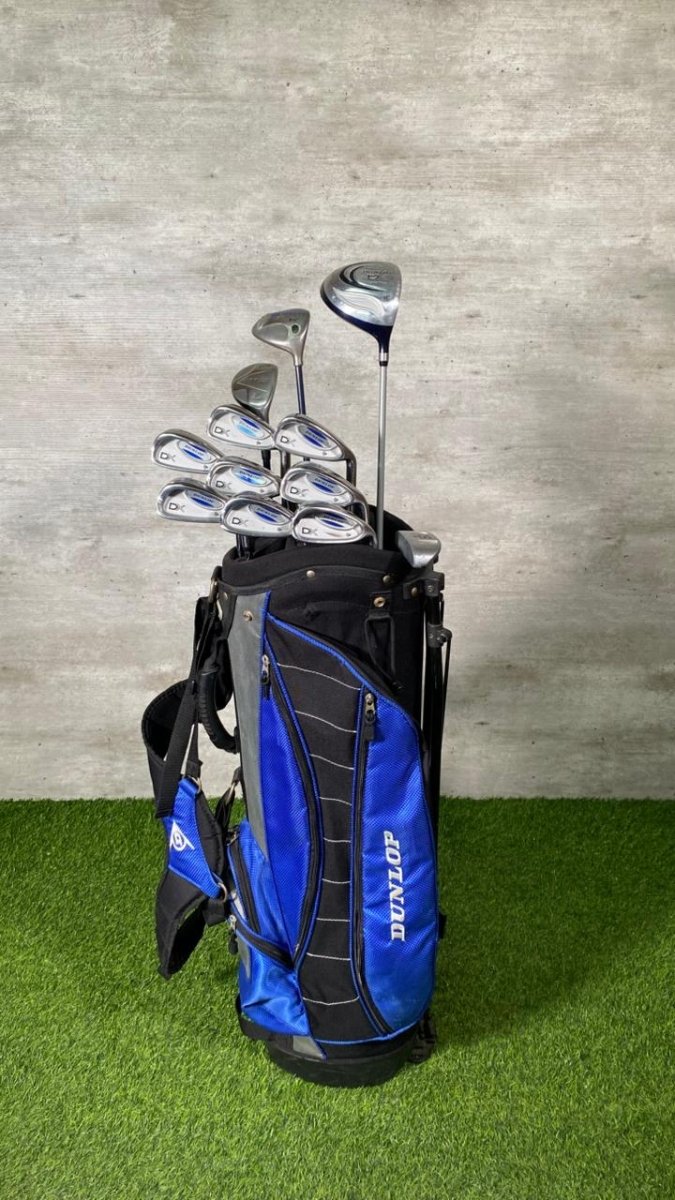 Golf clubs in a blue and black bag on a grassy surface with a gray wall background