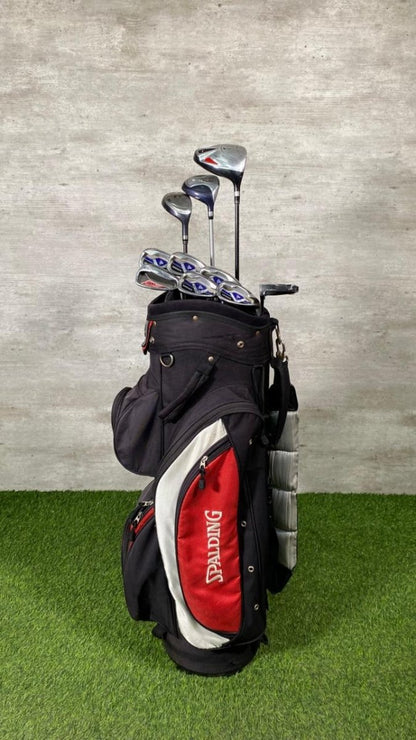 Golf bag with clubs on a grassy surface against a concrete wall