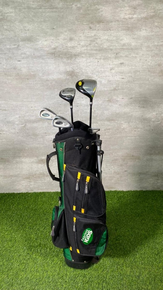 Golf clubs in a black and green bag on grass with a concrete wall background
