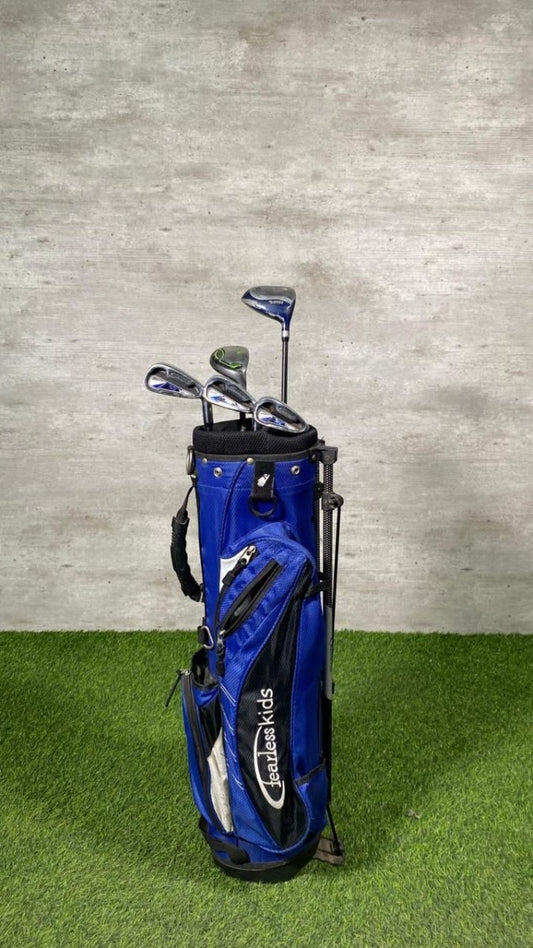 Blue golf bag with clubs on a grassy surface against a gray wall