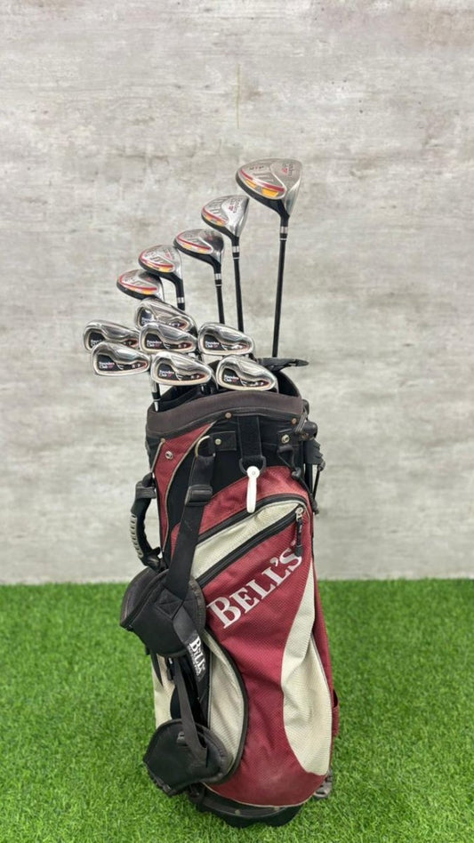Golf club set in a Bells bag on a grassy surface with a gray wall background