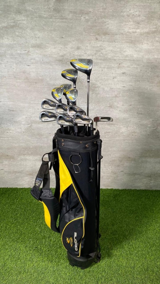 Golf club set in a black and yellow bag on grass with a gray wall background