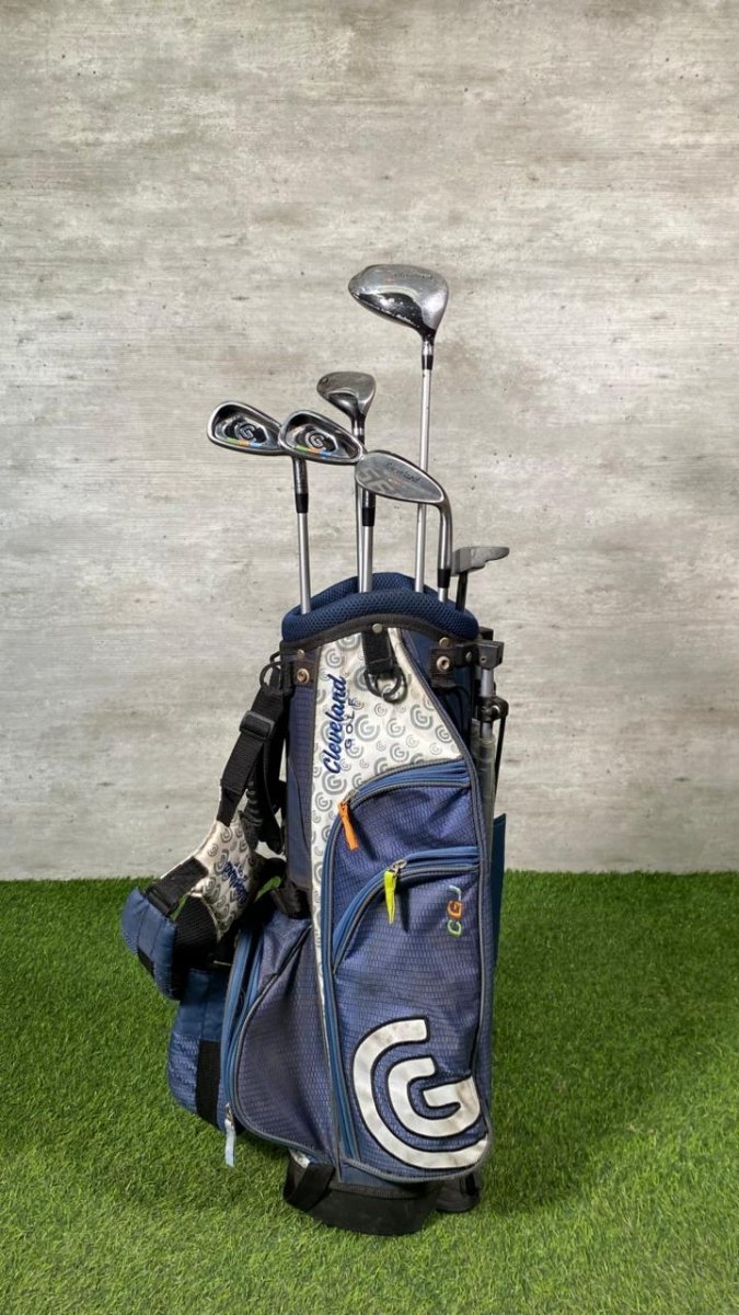 Set of golf clubs in a blue bag on a grassy surface with a gray concrete wall background