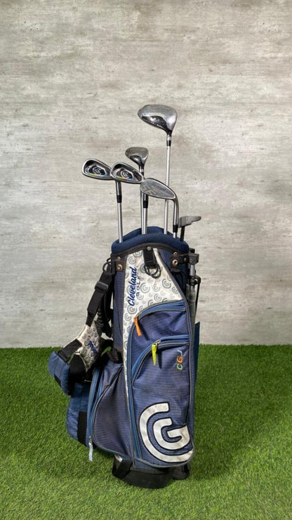 Set of golf clubs in a blue bag on a grassy surface with a gray concrete wall background