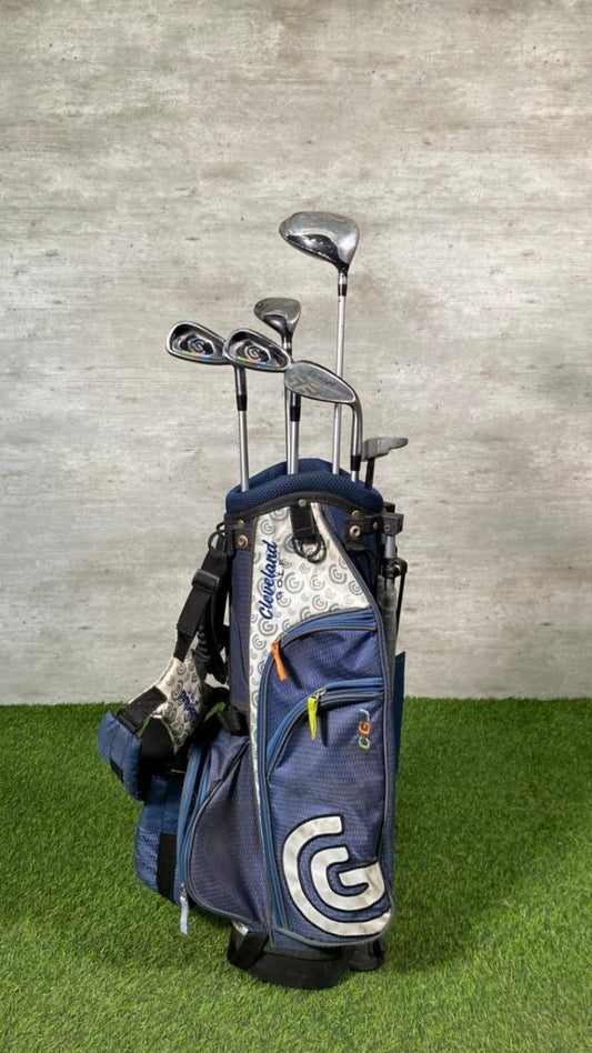 Set of golf clubs in a blue bag on a grassy surface with a gray concrete wall background