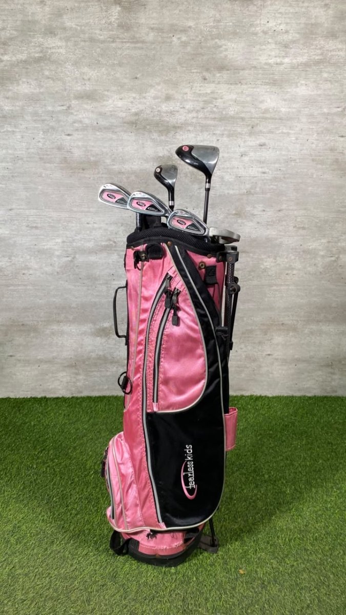 A pink and black Callaway golf bag filled with golf clubs, standing on artificial green turf against a textured gray wall.