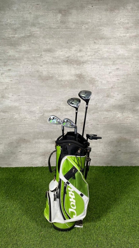 Golf clubs in a green and white bag on a grassy surface with a concrete wall background