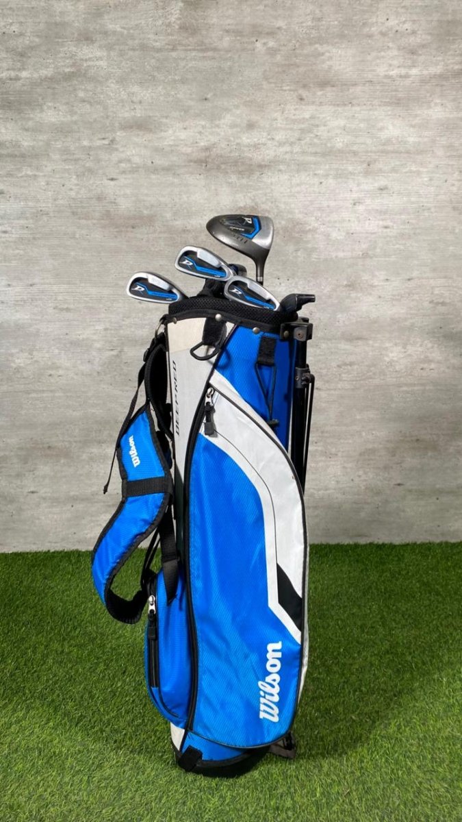 Blue golf bag with golf clubs against a gray wall.