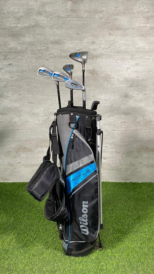 Golf clubs in a bag on a grassy surface with a concrete wall background
