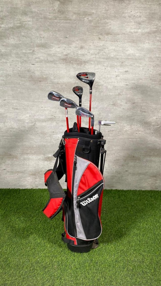 Golf clubs in a red and black bag on grass with a concrete wall background