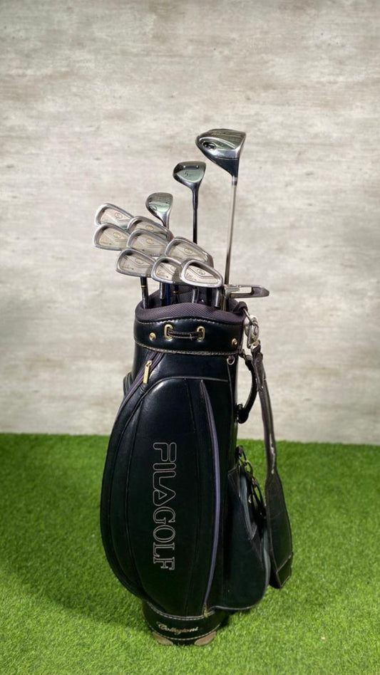 Golf club set in a black FILA GOLF bag on green grass with a gray wall background