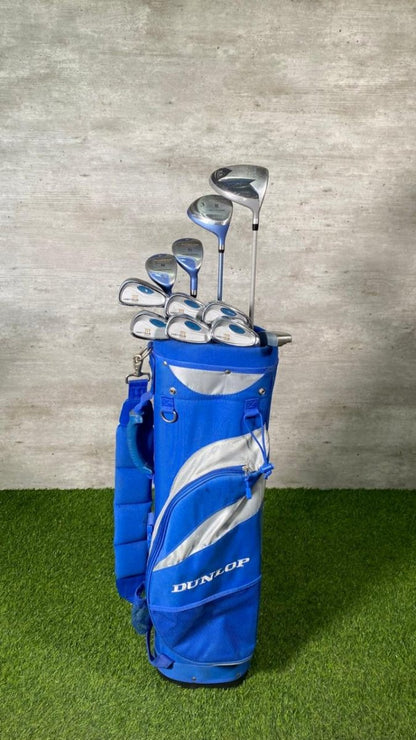 Set of golf clubs in a blue bag on a grassy surface with a concrete wall background