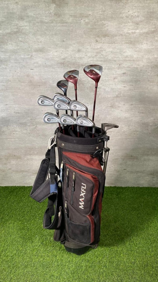 Golf clubs in a Maxfli bag on grass with a concrete wall background