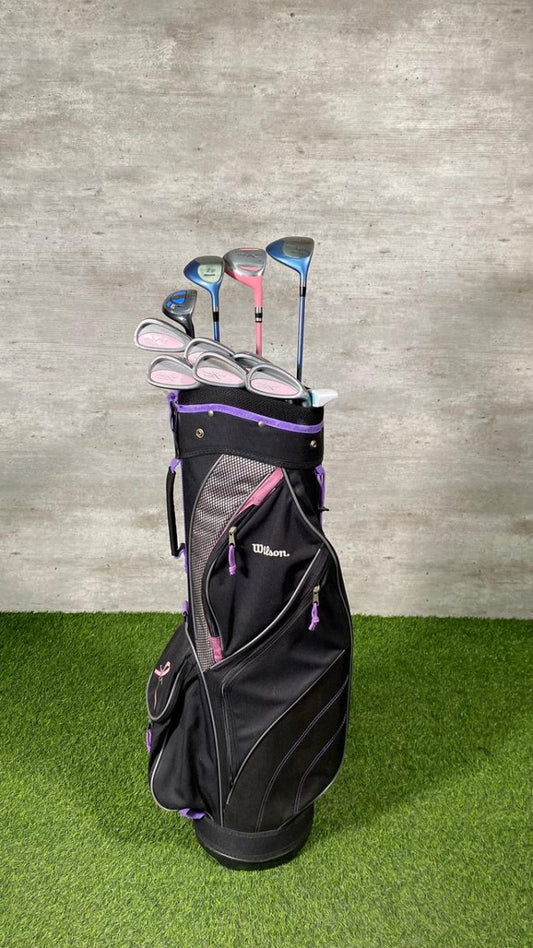 Golf clubs in a black bag on grass with a gray wall background