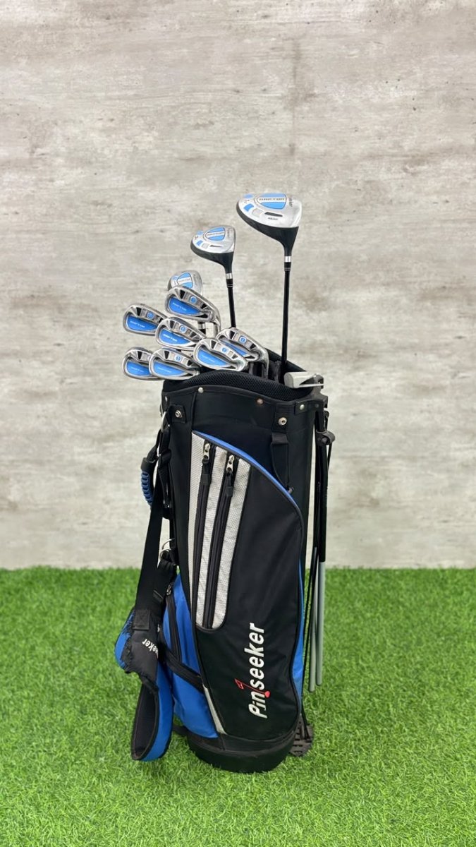 Golf clubs in a black and blue bag on grass with a gray wall background