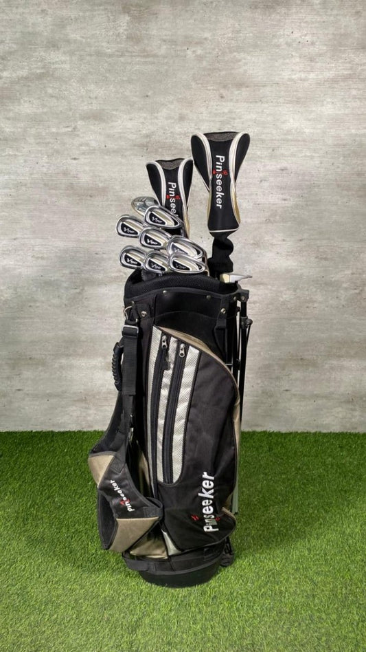 Golf clubs in a black bag on a grassy surface with a gray wall background