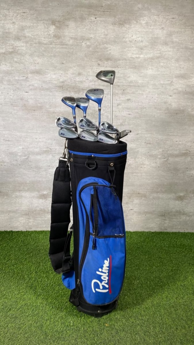 A blue and black golf bag filled with golf clubs, standing on artificial green turf against a textured gray wall. The bag features the brand name 'Pakrine' in white script with a red accent.