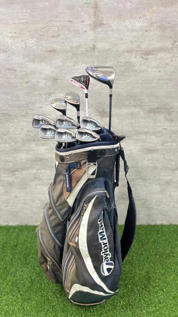 Golf clubs in a TaylorMade bag on a grassy surface with a gray concrete wall background