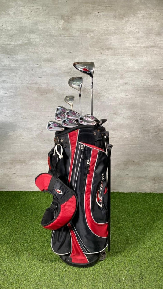 Black and red golf bag with golf clubs on a grassy surface and concrete wall background