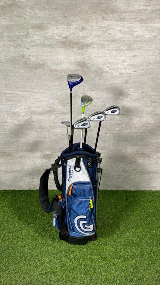 Golf clubs in a blue bag on a green surface with a gray wall background